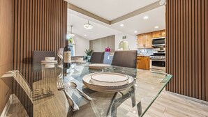 Un espace repas moderne avec une table en verre pour quatre personnes, un lambris en bois sur les murs et une cuisine en arrière-plan.