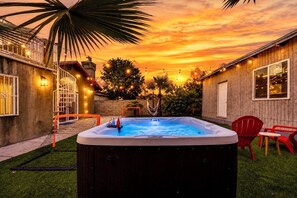 Ein Whirlpool im Garten mit Sonnenuntergangsblick, umgeben von einem Holenzaun, einer Palme und roten Stühlen.