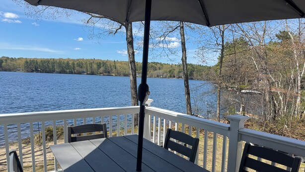 Eine Holzterrasse mit Tisch und Stühlen mit Blick auf einen See und einen Wald.
