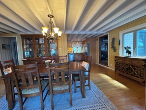 Ein Essbereich mit Holztisch und Stühlen, einer Chandelier und Blick auf die Küche sowie den Wohnbereich.