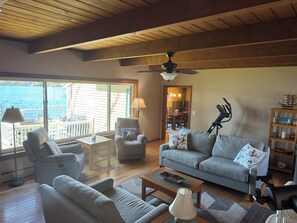 Ein geräumiges Wohnzimmer mit Blick aufs Wasser, einem Deckenventilator und einem Essbereich, der durch eine offene Tür sichtbar ist.