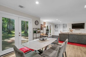 Ein modernes Wohnzimmer mit Essbereich, einer Couch, einem Fernseher und Blick ins Freie.