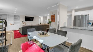 Una sala moderna con sofá, televisor y comedor con mesa y sillas.
