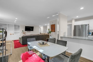 Ein modernes Wohnzimmer mit einer Couch, einem Fernseher und einem Essbereich mit Tisch und Stühlen.
