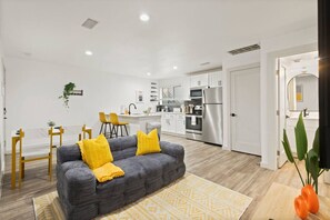 Ein modernes Wohnzimmer mit einer Couch, gelben Kissen, einem gemusterten Teppich und einer Küche im Hintergrund.