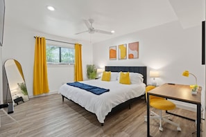 Ein modernes Hotelzimmer mit Bett, Schreibtisch, Stuhl und Deckenventilator.