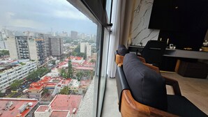 A high-rise room with a city view, a sofa, a TV, and a desk with a chair.