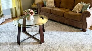 A living room with a brown leather sofa, a glass coffee table with a vase, a floor lamp, and yellow curtains. - Work Trip & Family Friendly - 3BR House in Historic Sayles. Long Term Stays (Abilene)