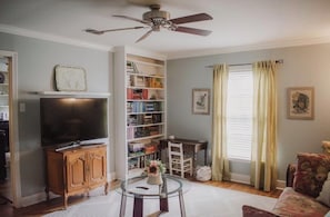 A living room with a television, bookshelves, a ceiling fan, a dining table, and a sofa.
