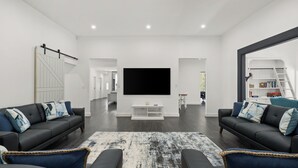 Ein modernes Wohnzimmer mit einem großen Flachbildfernseher, zwei blauen Sofas, einem gemusterten Teppich und einem Bücherregal mit Büchern und einer Bibliothekstreppe.
