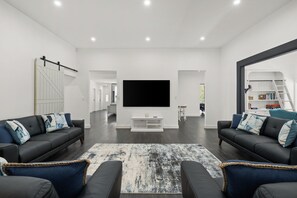 A modern living room with a large flat-screen TV, two sofas with blue cushions, a patterned rug, and a bookshelf with books and a ladder. - Farm stay in Falls Creek (Falls Creek)