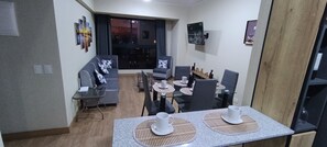 Una sala de estar moderna con un sofá, una mesa de comedor, sillas y un televisor montado en la pared.