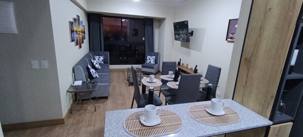 Una sala de estar moderna con un sofá, una mesa de comedor, sillas y un televisor montado en la pared.