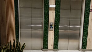 An elevator area with two elevators, a wooden wall, and a potted plant. - The yako and whiteman department (Lima)