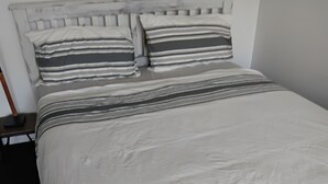 Ein Bett mit grau-weiß gestreifter Bettdecke, einem Holzkopfende und einem schwarzen Boden.