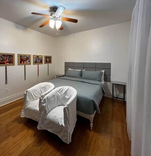 Ein Schlafzimmer mit Bett, Sessel, Deckenventilator und Bildern an der Wand.