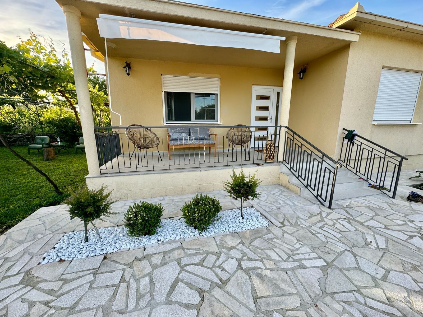 A covered outdoor seating area with a stone patio, a small tree, and a white door.