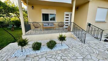 A covered outdoor seating area with a stone patio, a small tree, and a white door.