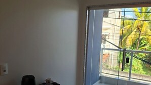 A modern room with a glass door leading to a balcony, a small white console table with a speaker and a tray of items, and a clean, tiled floor.