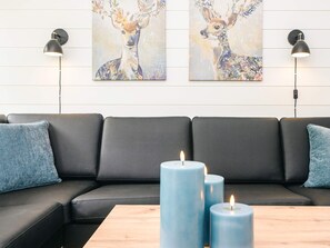 A modern living room with a black leather sofa, two wall-mounted lamps, and three blue candles on a wooden table. - 4 Star Holiday Home in Aabenraa (Aabenraa)