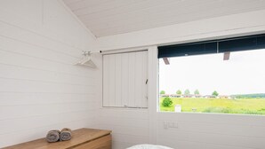 A bedroom with a wooden dresser, a bed with white bedding, a window with a view of a green field and houses, and a white door. - 4 Star Holiday Home in Aabenraa (Aabenraa)