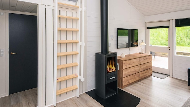 A modern interior with a black wood-burning stove, a wooden ladder, and a TV mounted on the wall. - 4 Star Holiday Home in Aabenraa (Aabenraa)