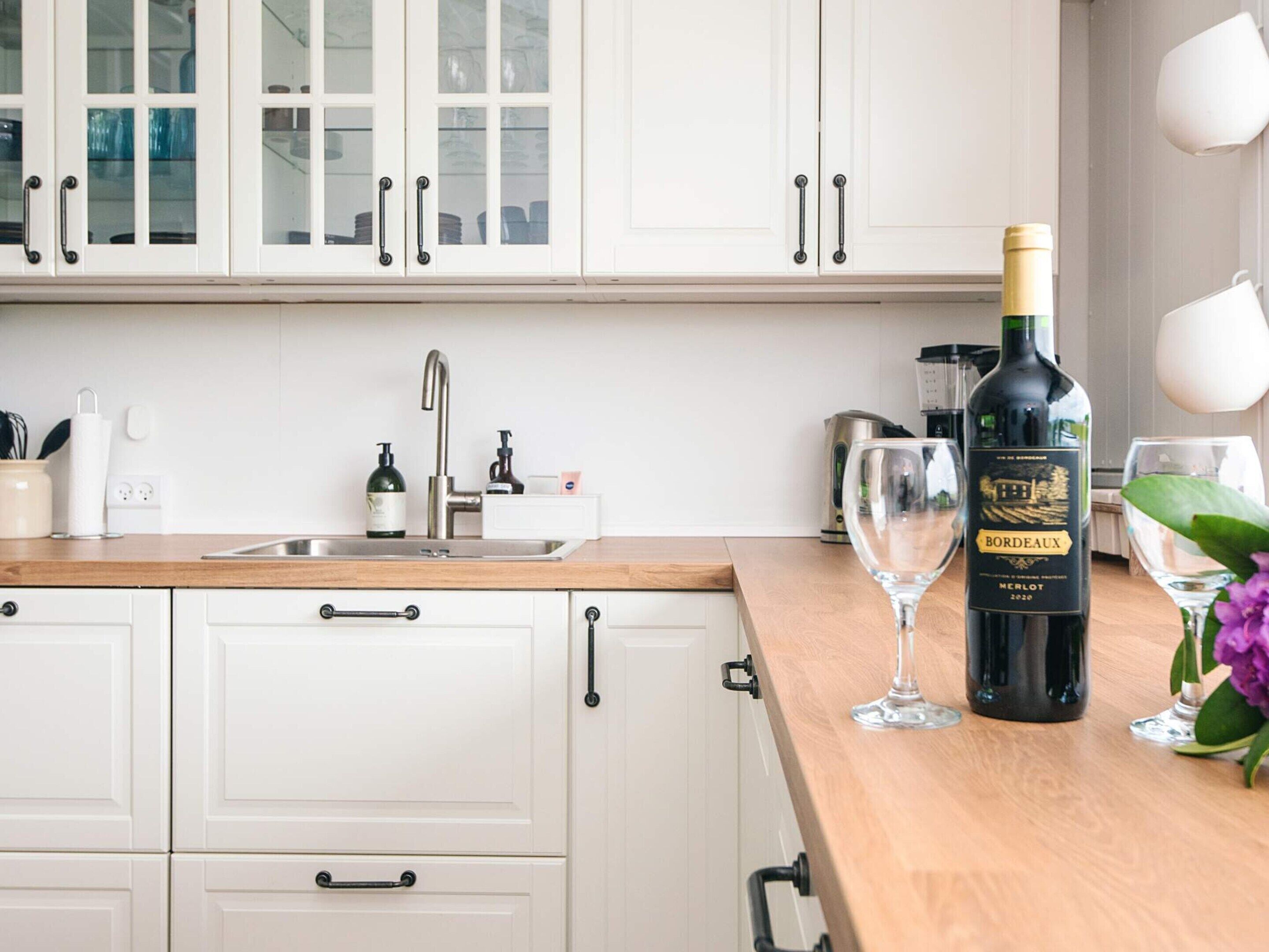 A kitchen with white cabinets, a wooden countertop, a sink, a wine bottle, and a glass.