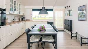 A modern kitchen with white cabinets, a dining table with chairs, a pendant light, and a view of the outdoors through a window. - 4 Star Holiday Home in Aabenraa (Aabenraa)