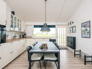 A modern kitchen with white cabinets, a dining table with chairs, a pendant light, and a view of the outdoors through a window. - 4 Star Holiday Home in Aabenraa (Aabenraa)