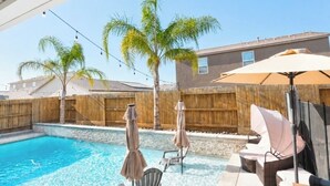 Ein Pool mit Liegestühlen und Sonnenschirmen, umgeben von einem Holzzaun und Palmen.