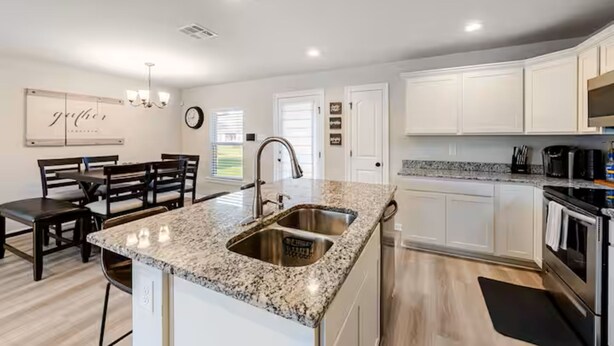 A kitchen with white cabinets, granite countertops, stainless steel appliances, and a dining area with dark wooden chairs.