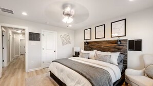 A bedroom with a bed, a wooden headboard, a nightstand, a chair, and framed artwork on the wall.