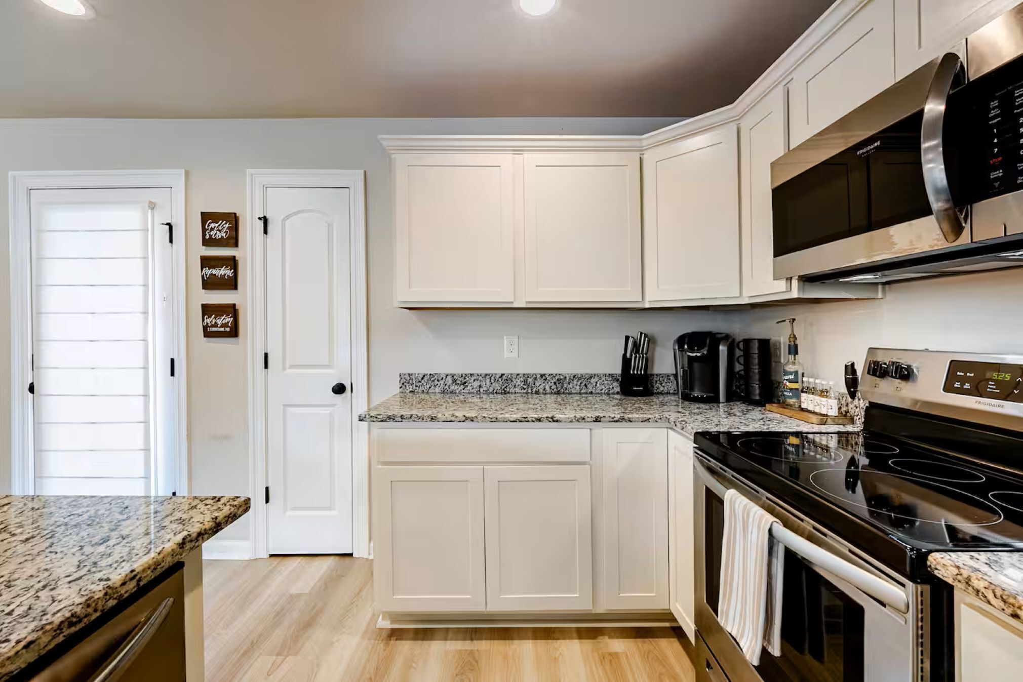 A kitchen with white cabinets, granite countertops, a stainless steel microwave, and a black stove.