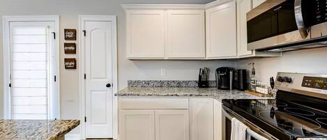 A kitchen with white cabinets, granite countertops, a stainless steel microwave, and a black stove.