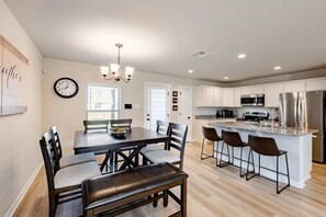 Une cuisine moderne équipée d’appareils électroménagers en acier inoxydable, un coin repas avec une table et des chaises en bois, et un lustre.