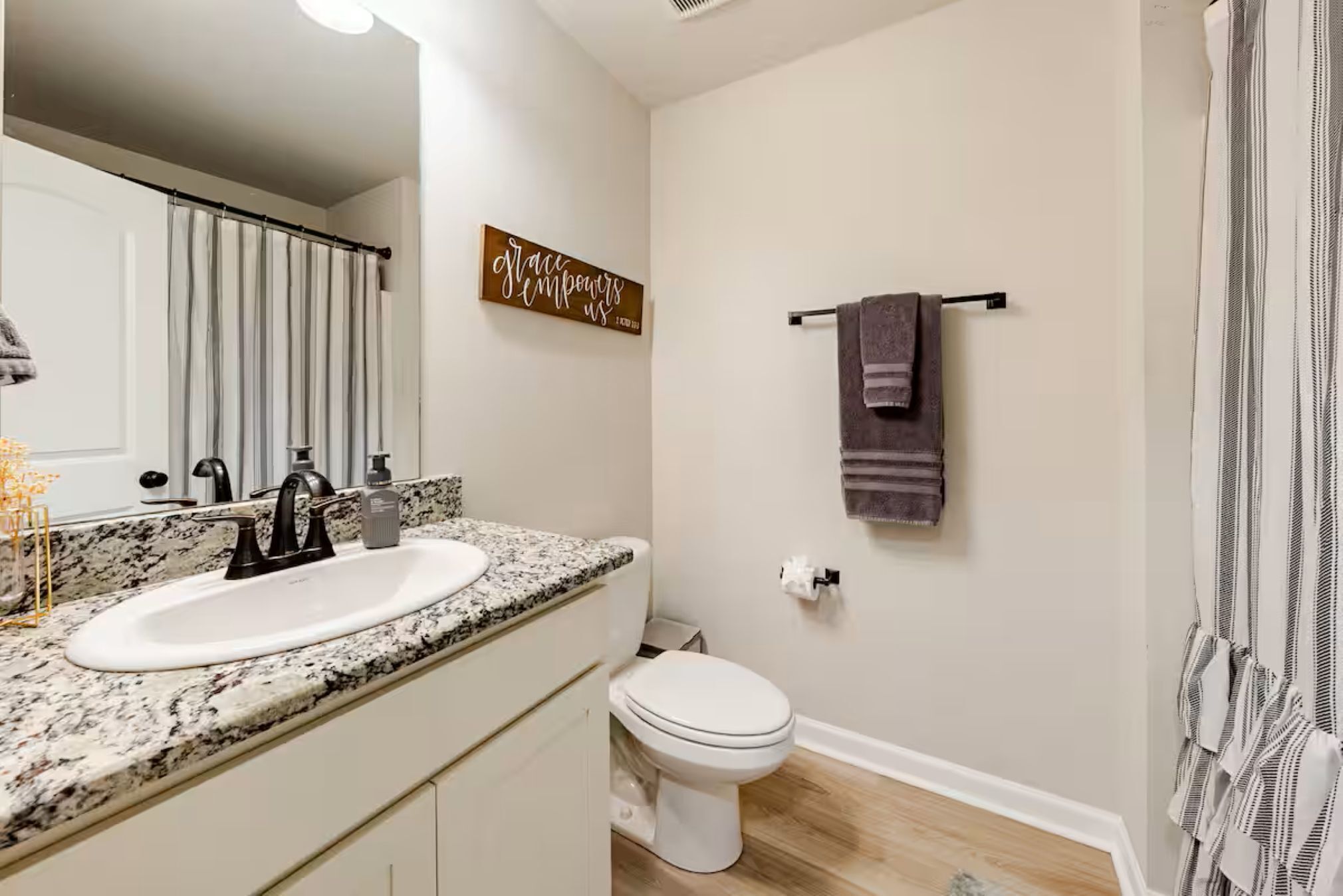 Une salle de bain avec un lavabo blanc, un robinet noir et des toilettes. On y trouve un porte-serviettes avec une serviette et un panneau accroché au mur.