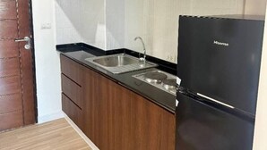Eine Küche mit dunklen Holzschränken, einem schwarzen Kühlschrank und einer Edelstahl-Spüle.