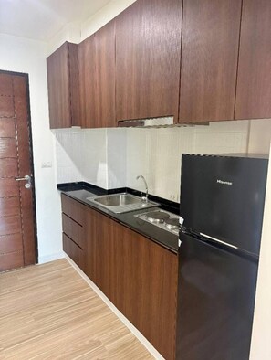 Eine Küche mit dunklen Holzschränken, einem schwarzen Kühlschrank und einer Edelstahl-Spüle.