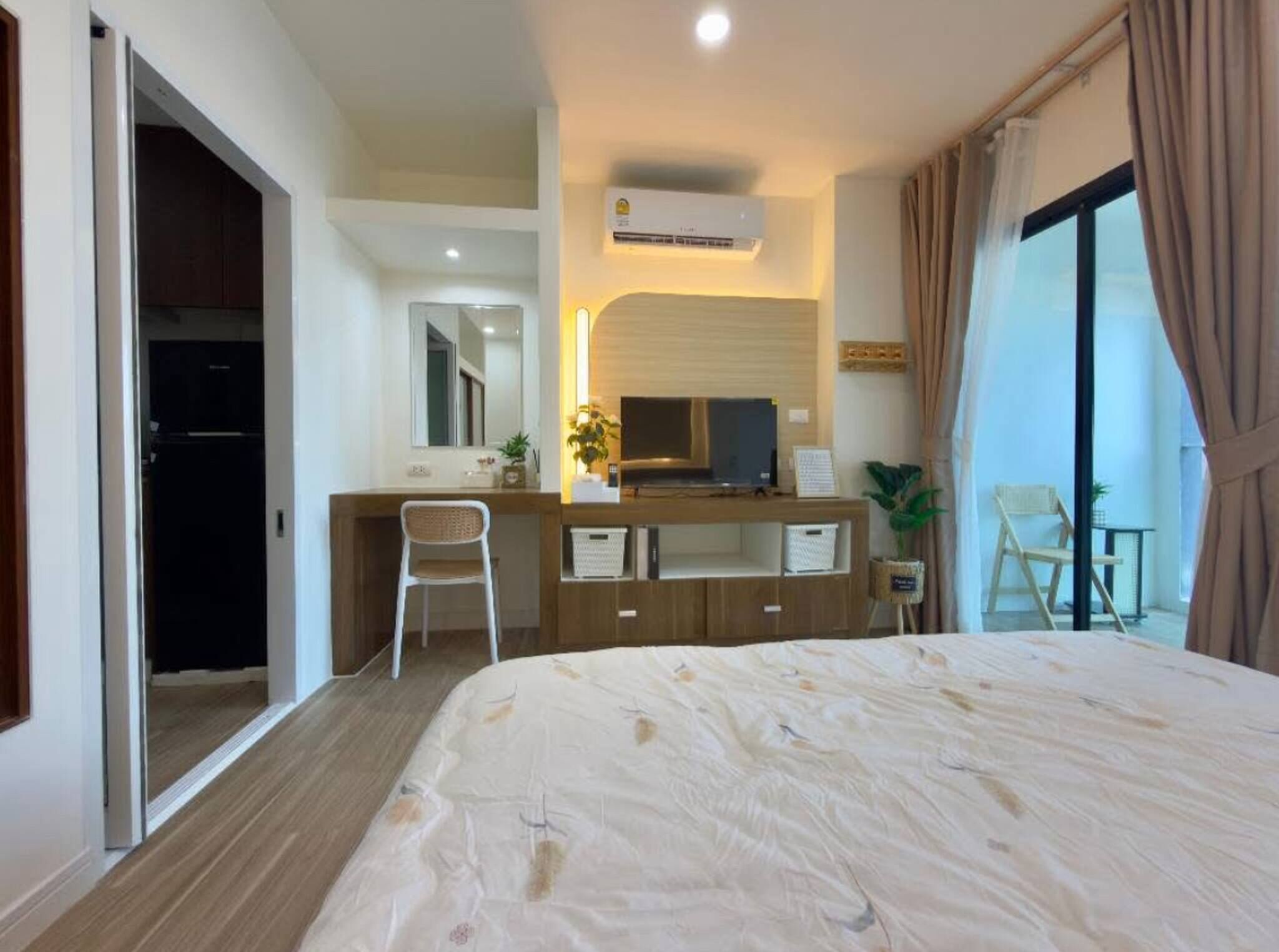 A hotel room with a bed, a desk with a chair, a television, and a sliding door leading to a balcony.