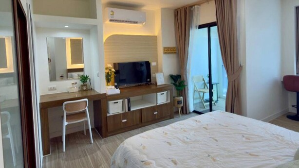 Ein Hotelzimmer mit einem Bett, einem Schreibtisch mit Fernseher, einem Sessel, einer Pflanze und einer Schiebetür zum Balkon.
