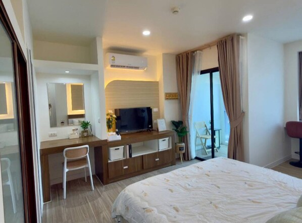 Ein Hotelzimmer mit einem Bett, einem Schreibtisch mit Fernseher, einem Sessel, einer Pflanze und einer Schiebetür zum Balkon.