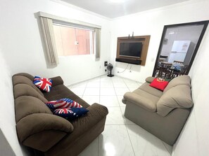 A living room with two sofas, a TV, and a window. - Complete house with private backyard. (Mogi das Cruzes)