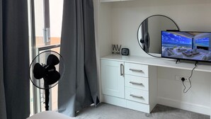 A hotel room with a bed, a desk with a TV, a fan, and a window with curtains. - One Bedroom Flat in Mailbox With Free Parking (Birmingham)