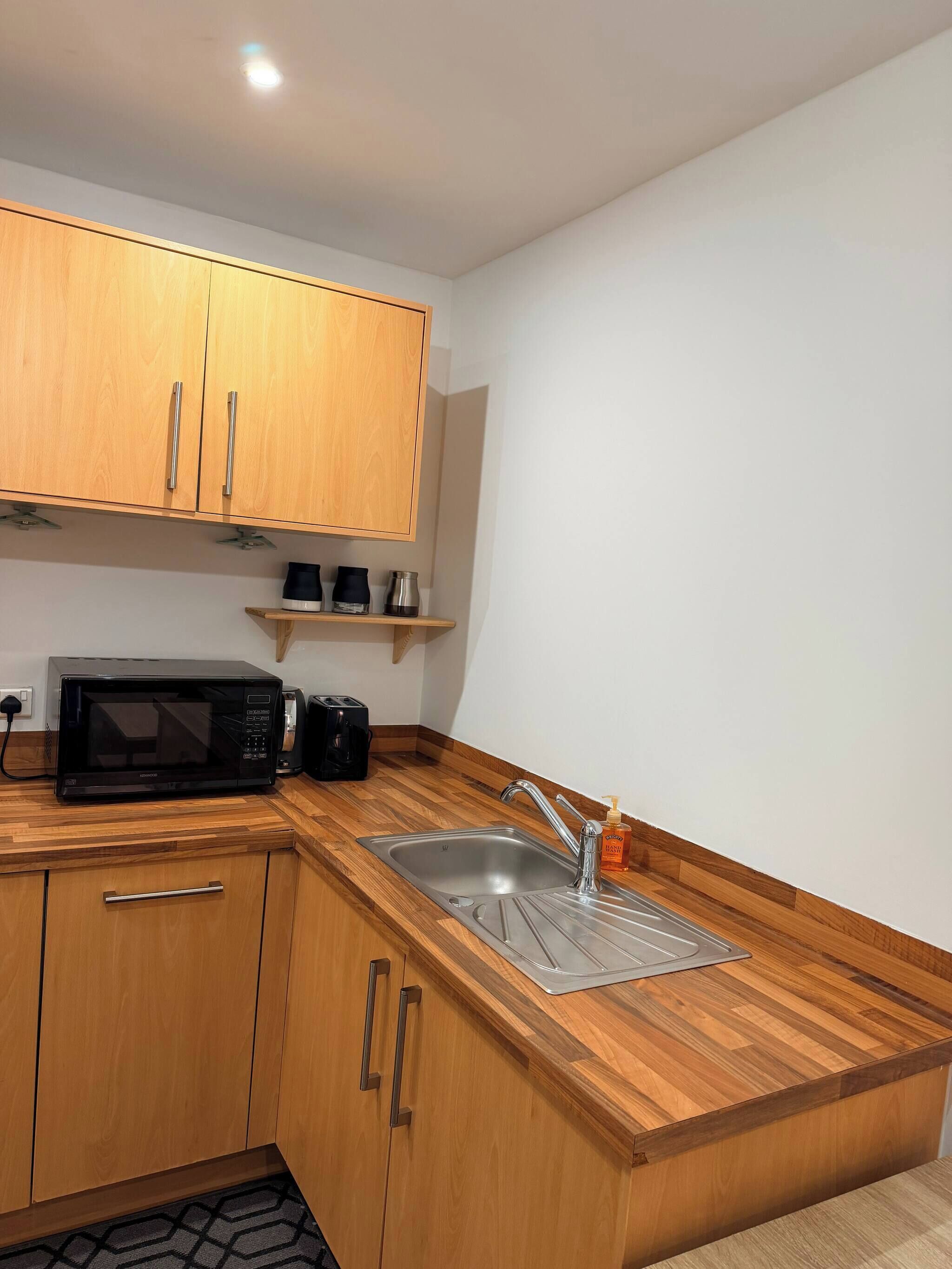 A compact kitchen with wooden cabinets, a stainless steel sink, a microwave, and a coffee maker.