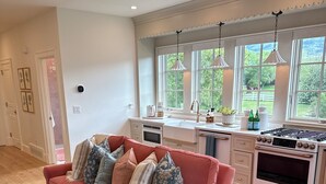A modern kitchen with a red sofa, ottomans, and a view of greenery outside. - Charming 1-bedroom studio cottage in delightful Fish Haven with AC (Fish Haven)