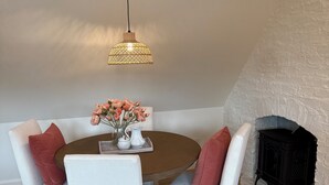 A dining area with a round table, white striped chairs, a vase with flowers, a hanging light fixture, and a stone fireplace. - Charming 1-bedroom studio cottage in delightful Fish Haven with AC (Fish Haven)