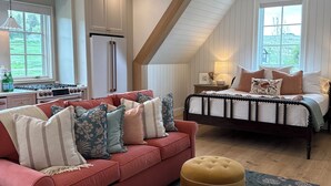 A cozy loft bedroom with a bed, a red sofa, and a kitchen area with a refrigerator and stove. - Charming 1-bedroom studio cottage in delightful Fish Haven with AC (Fish Haven)