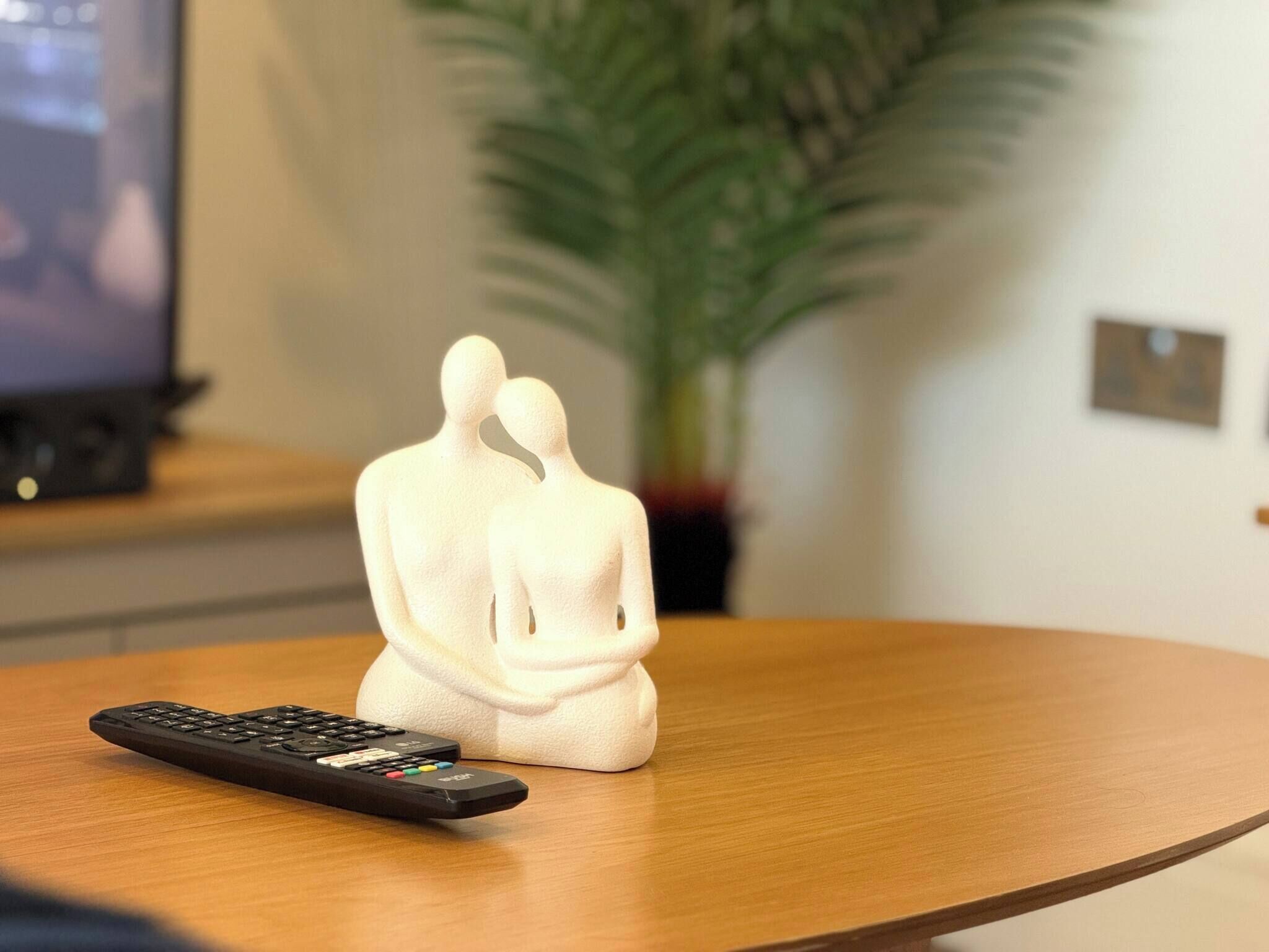 A remote control on a wooden table with a white sculpture of two figures.