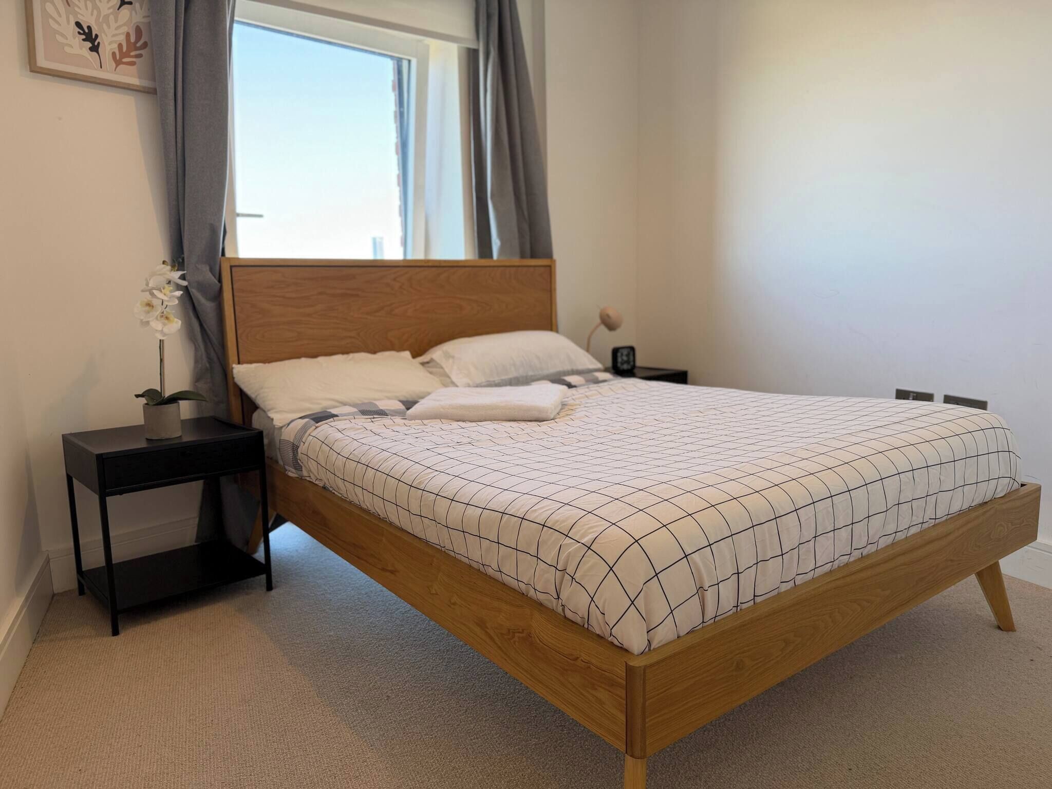 Un dormitorio con una cama de madera, una mesita de noche con lámpara y una ventana con cortinas.