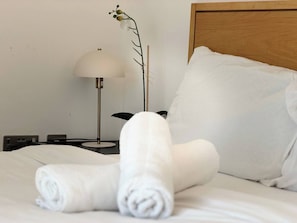 A neatly made bed with white linens, a rolled towel, a lamp, and a pillow on a wooden headboard. - One Bedroom Flat With Balcony Views in Birmingham (Birmingham)